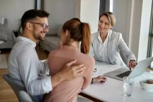 3.happy-real-estate-agent-using-laptop-while-talking-with-couple-meeting-office-300x200